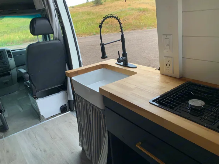 Explore this RV rental's modern van kitchen: farmhouse sink, black faucet, cooktop, and wood counters.. Mercedes Sprinter 2011
