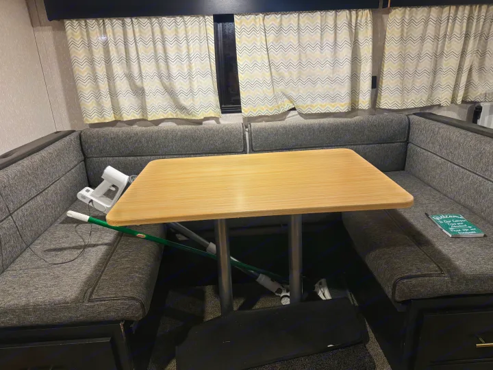 RV rental dinette area with gray upholstered benches, a light wood table, and chevron curtains. Cleaning supplies are visible.. Forest River Cherokee Grey Wolf 2022