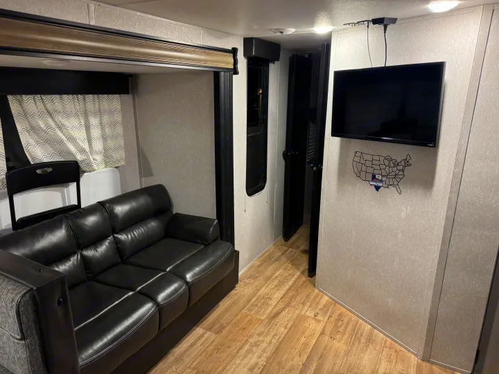 Modern rv rental living space featuring a black leather sofa, wall-mounted TV, and light wood-look flooring. Ready for your adventure!. Forest River Cherokee Grey Wolf 2022
