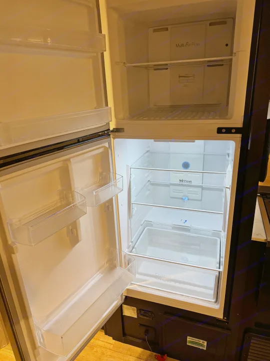 Open RV rental refrigerator, showcasing its empty interior with freezer (Multi Air Flow) and fridge (No Frost, crisper box).. Forest River Cherokee Grey Wolf 2022