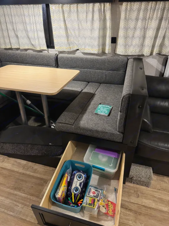 This RV rental interior shows a dinette with a guestbook, chevron curtains, and a pull-out drawer stocked with games & art supplies.. Forest River Cherokee Grey Wolf 2022