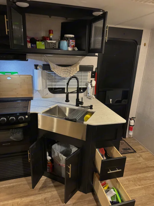 Modern RV rental kitchen featuring a farmhouse sink, oven, smart storage, and black cabinetry. Fully equipped for your travel adventures!. Forest River Cherokee Grey Wolf 2022
