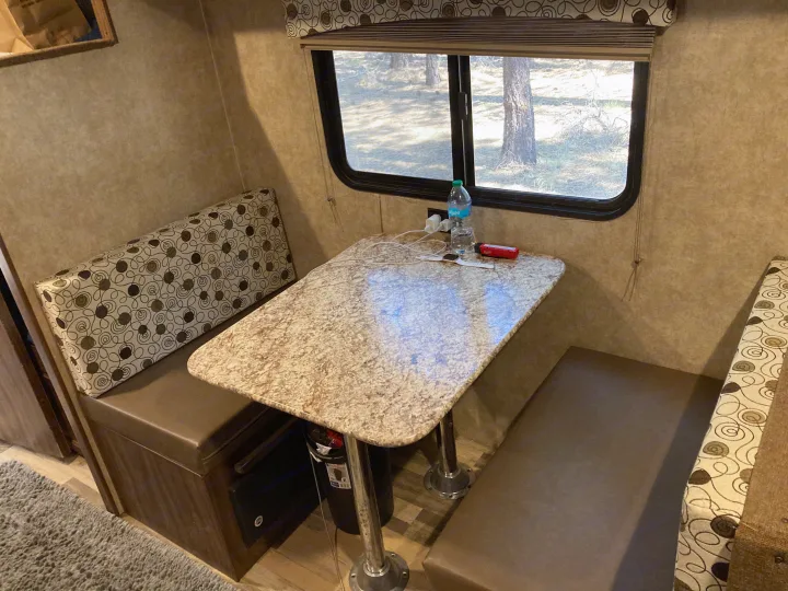 Cozy RV rental dinette featuring a patterned table, booth benches, and a window view of trees for comfortable travels.. Clipper 17BH 2018