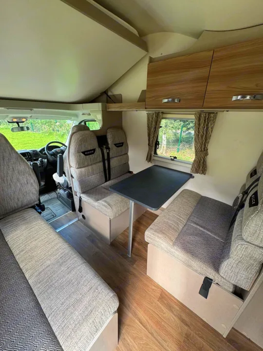 This rv rental interior features a dining area with a table and bench seats, plus an overhead bed for cozy travels.. Swift Edge 486 2024
