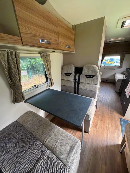 Cozy RV rental dining space: table, patterned seats with seatbelts, overhead storage, and wood-look floor.. Swift Edge 486 2024