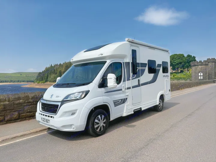 White Xplora motorhome RV rental parked on a scenic road overlooking a reservoir, ideal for outdoor adventures.. Moto-Trek Xplora FDB 2025