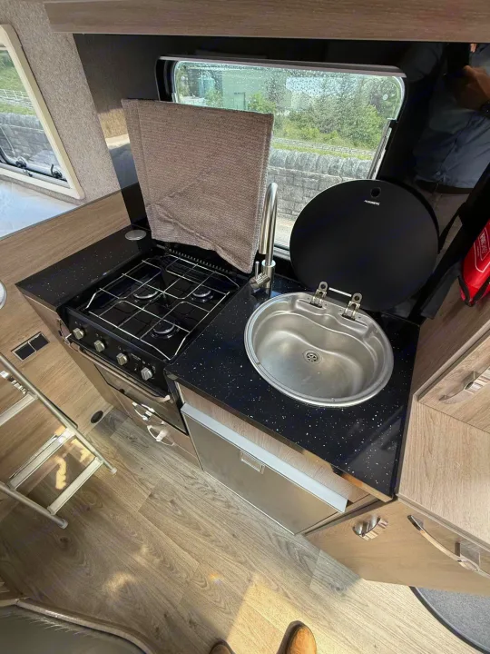 Inside a modern RV rental: a compact kitchen featuring a stove, oven, sink, and under-counter fridge.. Moto-Trek Xplora FDB 2025