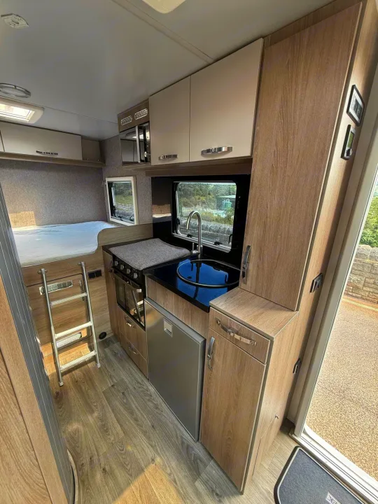 Modern rv rental interior: compact kitchen (sink, hob, oven, fridge), cozy bunk bed area with ladder, and overhead cabinets.. Moto-Trek Xplora FDB 2025