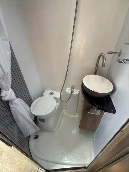 This RV rental bathroom offers a compact toilet, vessel sink, and shower with a curtain. Ideal for travel.. Moto-Trek Xplora FDB 2025