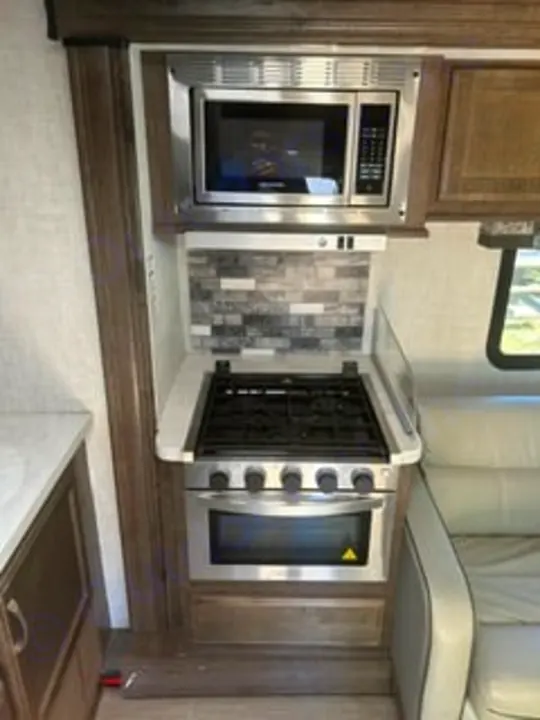 Compact RV rental kitchen with stainless steel microwave, gas stovetop, oven, and a modern tiled backsplash.. Gulf Stream Conquest 2022
