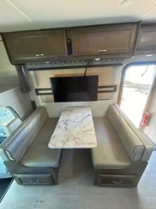 RV rental interior: A cozy dinette with bench seats, a white marble table, wall-mounted TV, and overhead cabinets.. Gulf Stream Conquest 2022