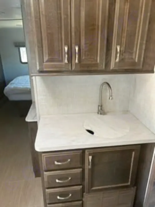 Explore this RV rental's modern interior! It features a functional kitchen with sink, wood cabinets, and a peek into the cozy bedroom.. Gulf Stream Conquest 2022