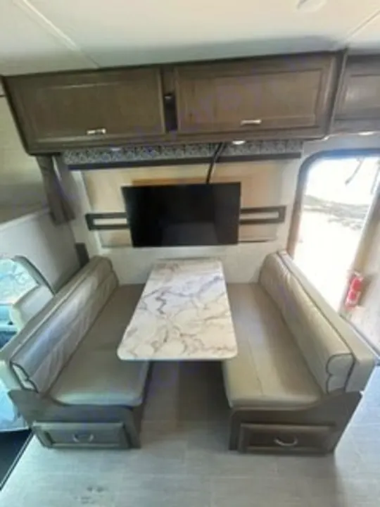 Your RV rental's inviting dinette: light benches, a modern table, and TV for comfort on the open road.. Gulf Stream Conquest 2022