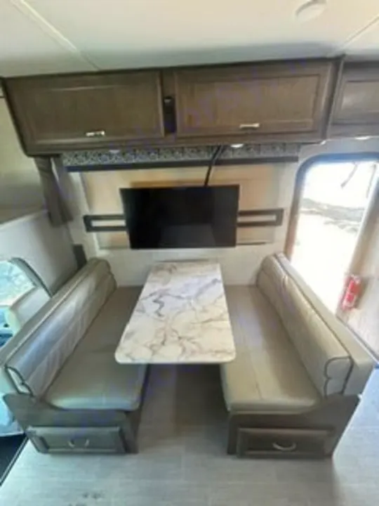 This RV rental interior features a bright dinette with two cushioned benches, a marble-look table, and a wall-mounted TV.. Gulf Stream Conquest 2022