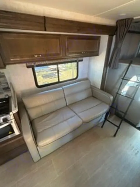 This inviting RV rental interior features a light-colored sofa, window with a view, a partial kitchen, and a bunk ladder.. Gulf Stream Conquest 2022