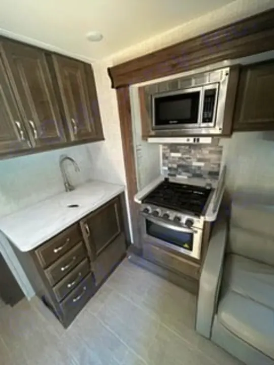Modern RV rental kitchen interior: stainless steel microwave, stovetop/oven, sink, and wood-look cabinets. Ready for your next adventure!. Gulf Stream Conquest 2022
