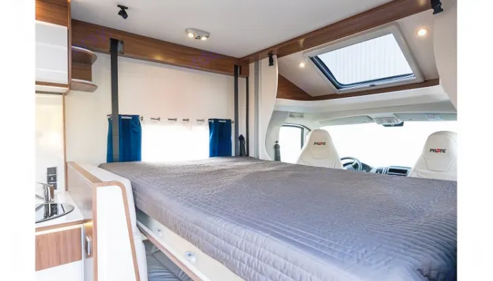 Spacious RV rental interior featuring a large bed, compact kitchen, and front cab with a bright skylight above.. PILOTE P726 C 2026