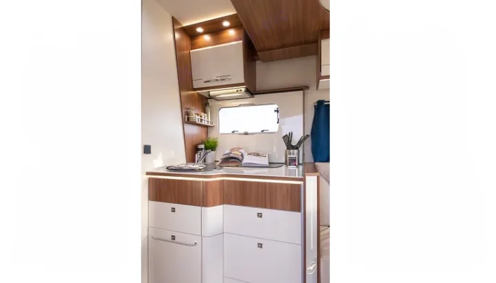 A bright, modern RV rental kitchen, featuring sleek wood and white cabinetry, a sink, stovetop, and ample storage for cooking on the go.. PILOTE P726 C 2026