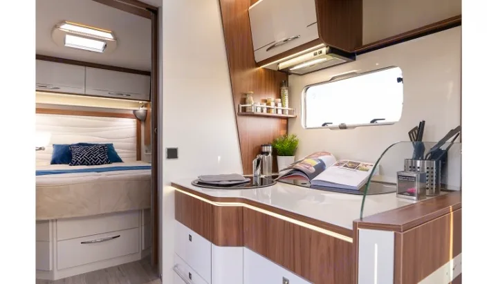 This RV rental interior showcases a modern kitchen with illuminated counters, spices, and a bright window, next to a comfortable bedroom.. PILOTE P726 C 2026