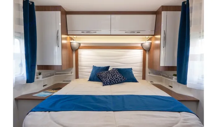 Spacious and cozy RV rental bedroom with a large bed, blue accents, reading lights, and convenient storage.. PILOTE P726 C 2026