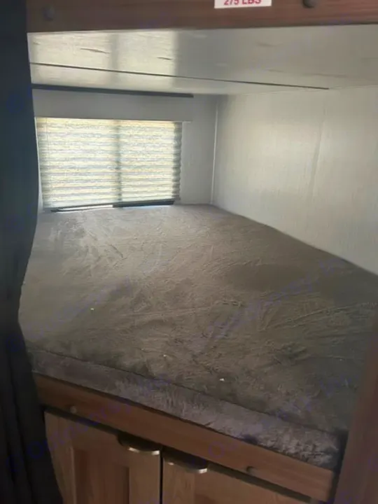 Inside this RV rental, find a comfortable lower bunk bed with dark grey bedding, window, and storage. Upper bunk support visible.. Cruiser RV MPG 2023