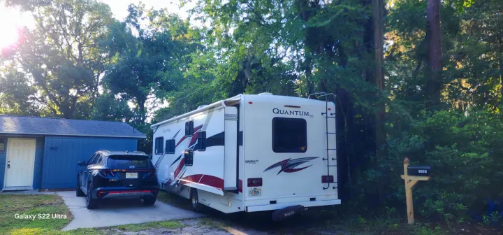 White Quantum SE RV rental parked with a black SUV at house 1821, surrounded by lush trees.. Thor Quantum 2021