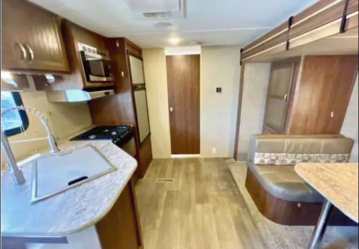 RV rental's inviting interior: functional kitchen, comfortable dinette seating, and stylish wood-grain flooring for your next trip.. Coleman 2305QB 2017