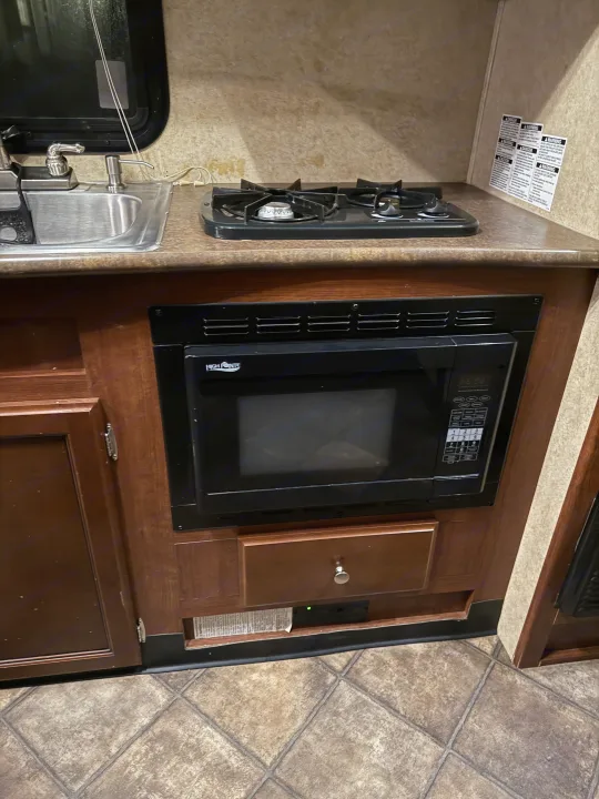 Compact RV rental kitchen featuring a sink, two-burner stovetop, and built-in microwave.. Evergreen RV Ascend 2015