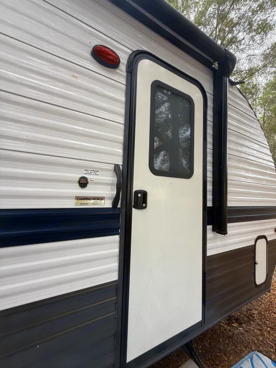Gulf Stream RV rental side, showing its door, awning, and textured paneling. Ready for your camping trip!. Gulf Stream Enlighten 2021