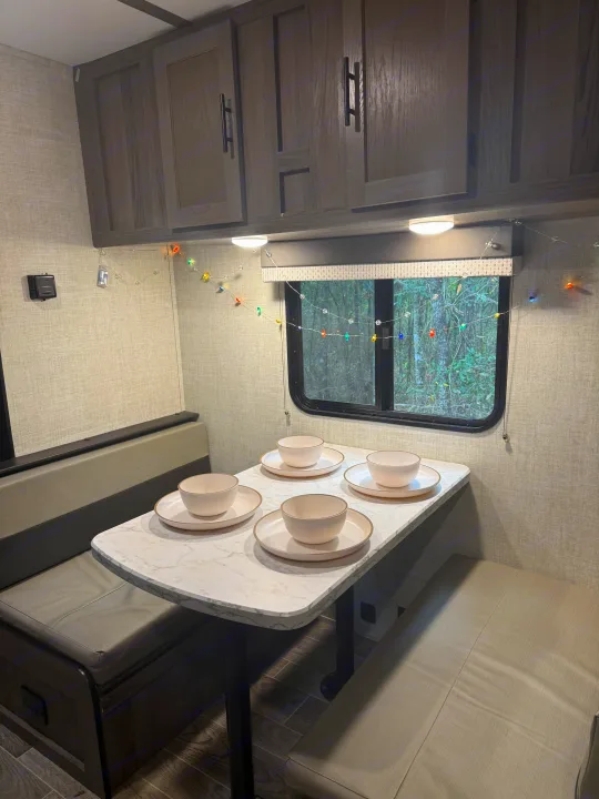 Cozy RV rental dinette with four place settings, overhead cabinets, and decorative lights, perfect for meals on the road.. Gulf Stream Enlighten 2021