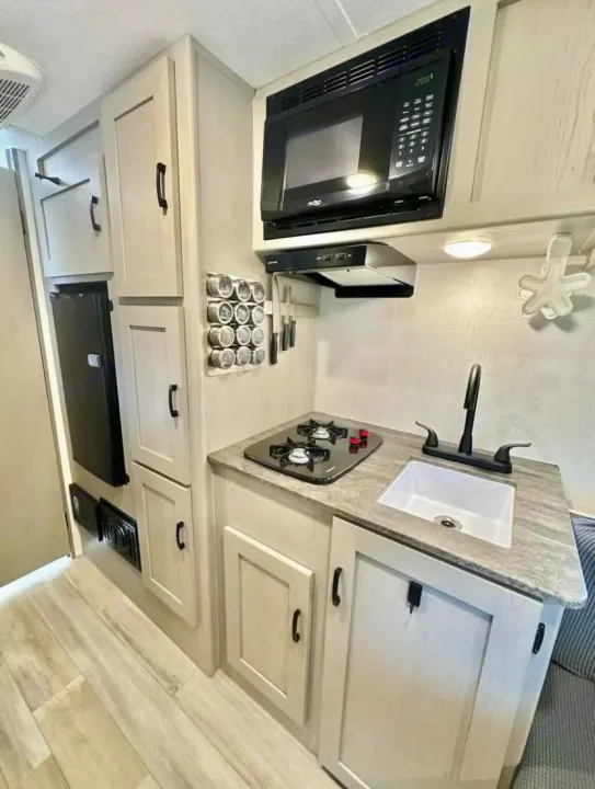 Modern RV rental kitchen: features microwave, sink, two-burner stove, fridge, and light wood cabinets for your travels.. Clipper 3K 2023