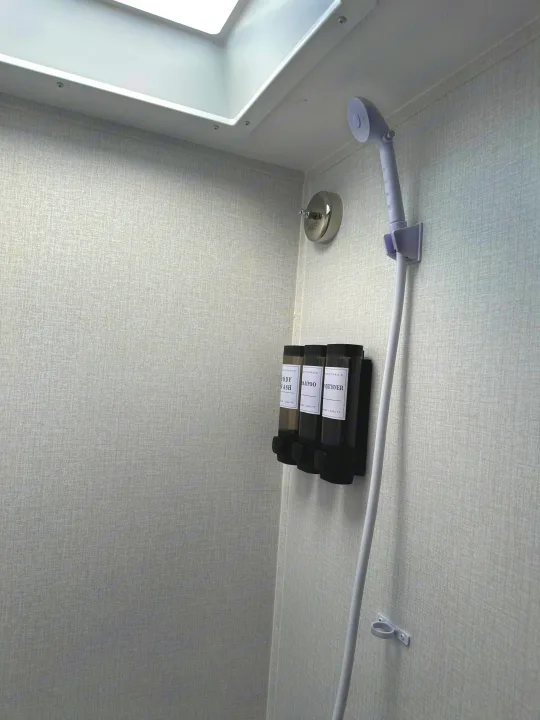 Inside an RV rental shower: skylight, handheld shower, and wall dispensers for body wash, shampoo, and conditioner.. Clipper 3K 2023