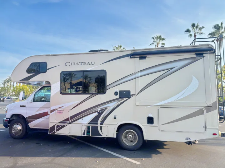 Side view of a tan Chateau motorhome rental, parked with palm trees, ready for your next adventure.. Thor Chateau 2019