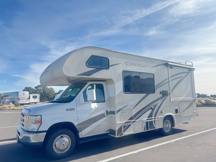 A grey and white Chateau E-350 Super Duty RV rental is parked outdoors under a blue, cloudy sky.. Thor Chateau 2019