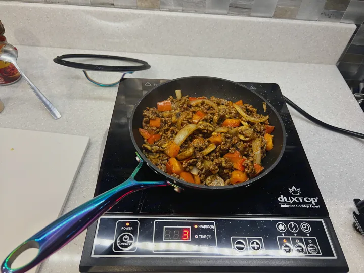 Sautéing ground meat, onions, peppers, and mushrooms on an induction cooktop, ideal for an RV rental kitchen.. Ram Promaster 1500 2020