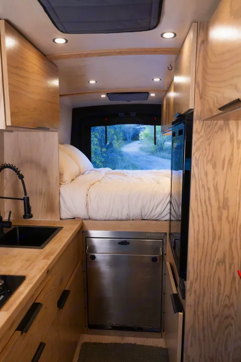 Cozy RV rental interior with bed, kitchen, and wood cabinetry for your next adventure. Enjoy van life with a view!. Ford Transit 2022