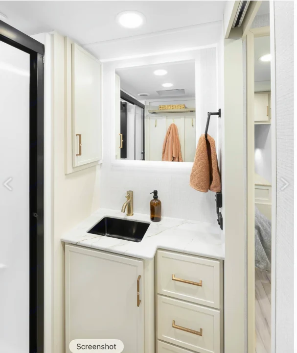 Modern RV rental bathroom vanity with sleek black sink, gold faucet, illuminated mirror, and cream storage cabinets.. Brinkley RV Model I 2025