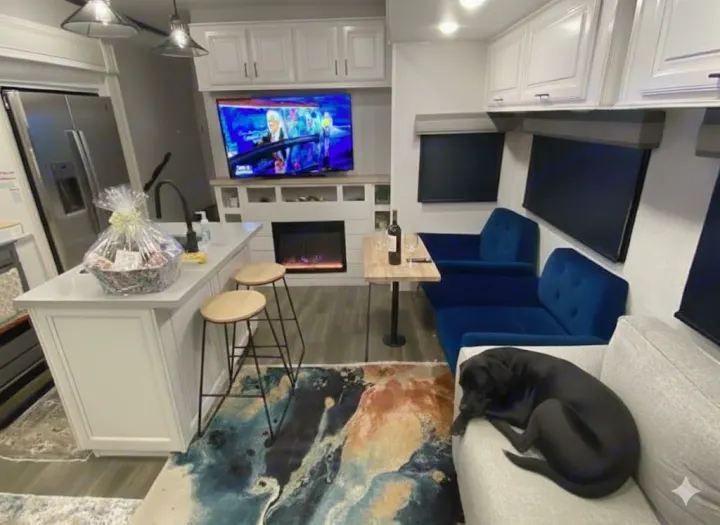 Cozy RV rental interior featuring a modern kitchen island, electric fireplace, living area, and a dog relaxing on the couch.. Highland Ridge RV Open Range 2024