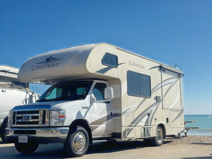 A Chateau RV rental, a Class C motorhome, parked on a sunny beach by the ocean, ready for travel adventures.. Thor Chateau 2019