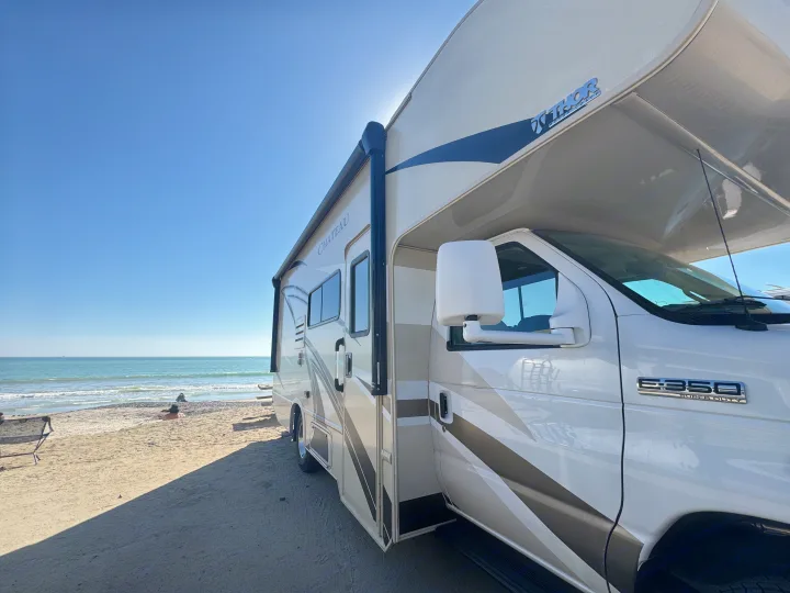 Thor Chateau RV rental on a sunny beach by the ocean, a person relaxing on the sand. Ideal for a coastal camping adventure.. Thor Chateau 2019