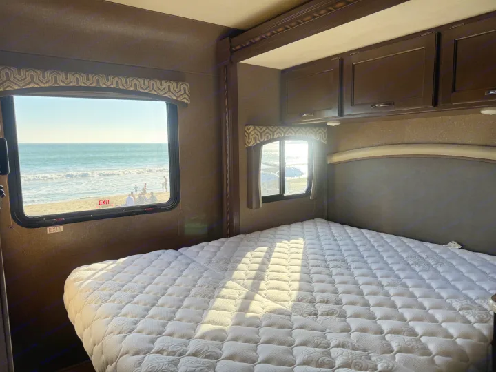 RV rental bedroom with a stunning ocean view, featuring a comfortable bed overlooking the beach and waves.. Thor Chateau 2019