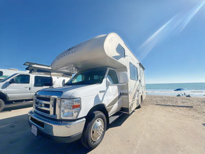 RV rental parked beachside on a sunny day. Ocean waves, people swimming. Great for a travel adventure by the sea.. Thor Chateau 2019