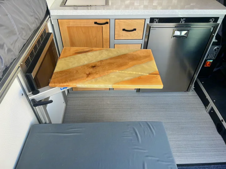 RV rental: Cozy camper van kitchen featuring a unique wood and resin table, fridge, microwave, and comfy bench.. Ram Promaster 1500 2020