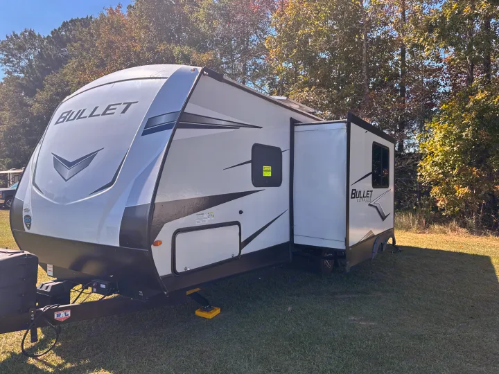 Experience outdoor adventures with this Bullet Ultra Lite RV rental, featuring a slide-out, parked on grass under a sunny sky.. Keystone RV Bullet Ultra Lite 2022