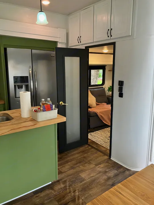 Modern RV rental kitchen with a green island, stainless steel fridge, and a door leading to a cozy living area with a sofa.. Highland Ridge RV Roamer 2017