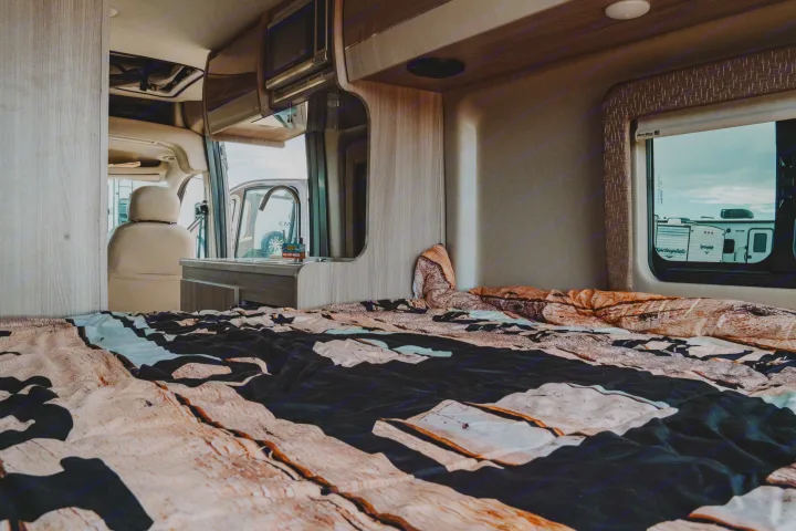 RV rental interior: bedroom with unique wood-patterned bed, kitchenette with microwave/sink, and outside view.. Thor Sequence 2021