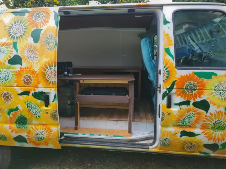 Bright sunflower-painted campervan with open side door reveals a mobile kitchen and simple sleeping area, ideal for rv rental adventures.. Ford Econoline 2007