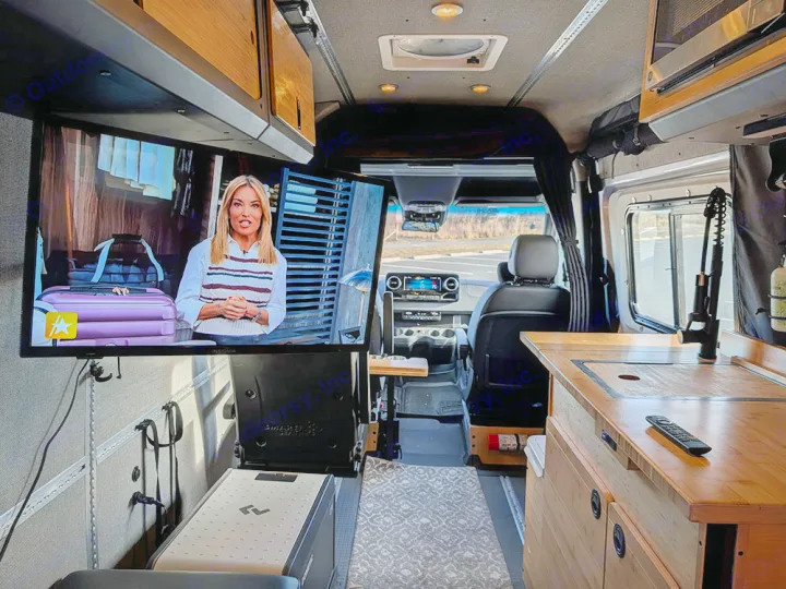 Inside a cozy rv rental camper van: TV on left, kitchen on right, and driver's cabin visible for mobile living.. Winnebago Adventure Wagon 2023