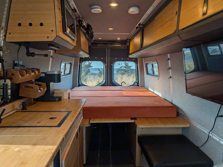 Modern RV rental interior with bamboo kitchenette, comfortable bed, and scenic ocean views, ideal for van life adventures.. Winnebago Adventure Wagon 2023