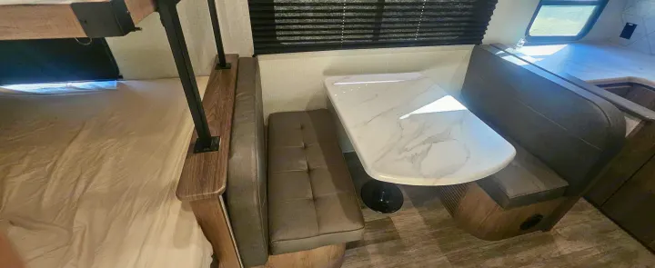 This RV rental interior offers a cozy dinette with a marble-look table, bench seating, and an adjacent bunk bed.. Grand Design Imagine AIM 2023